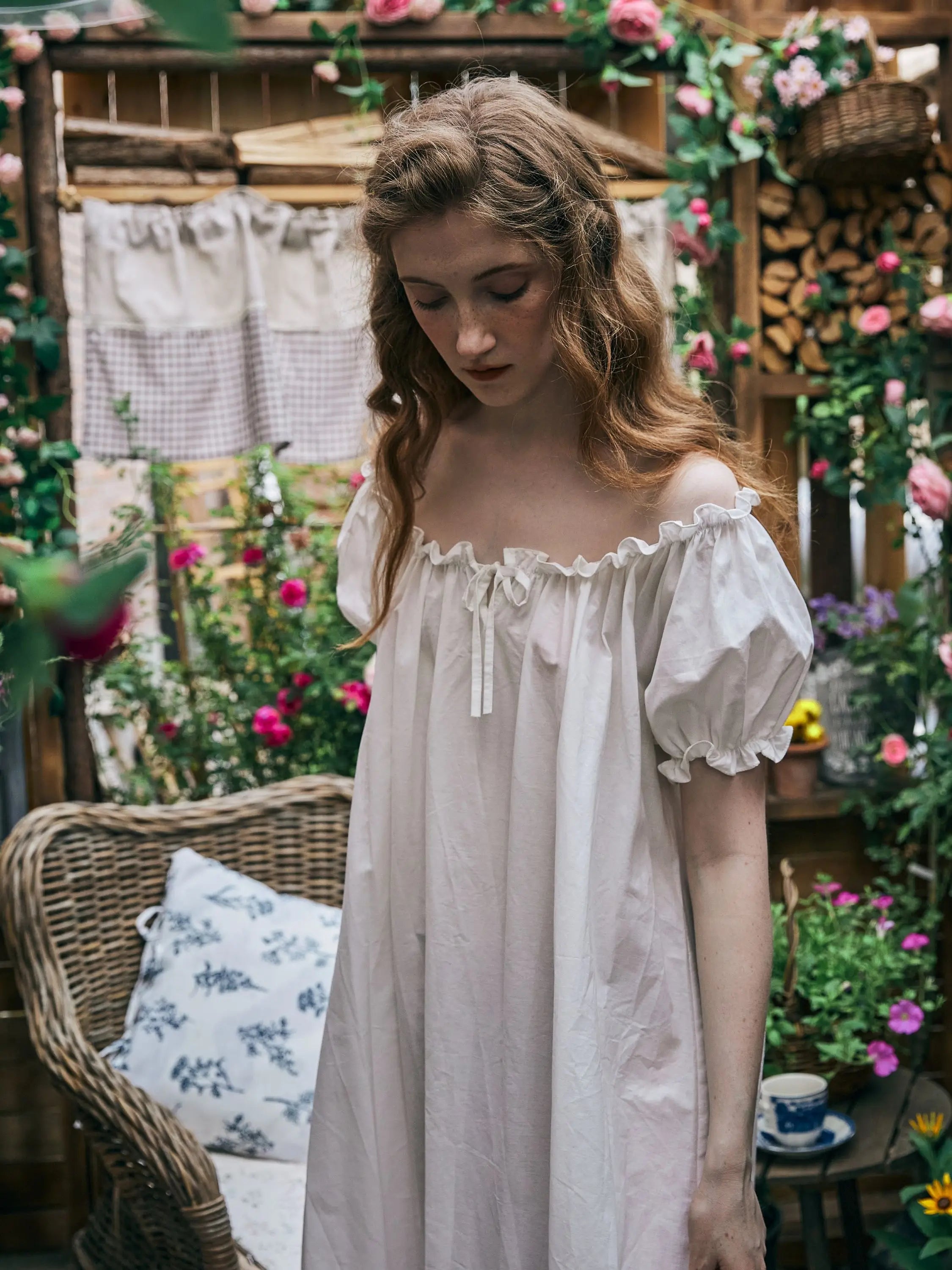 Woman wearing a vintage Victorian white cotton nightgown with a ruffled neckline and puff sleeves in a rustic garden setting.