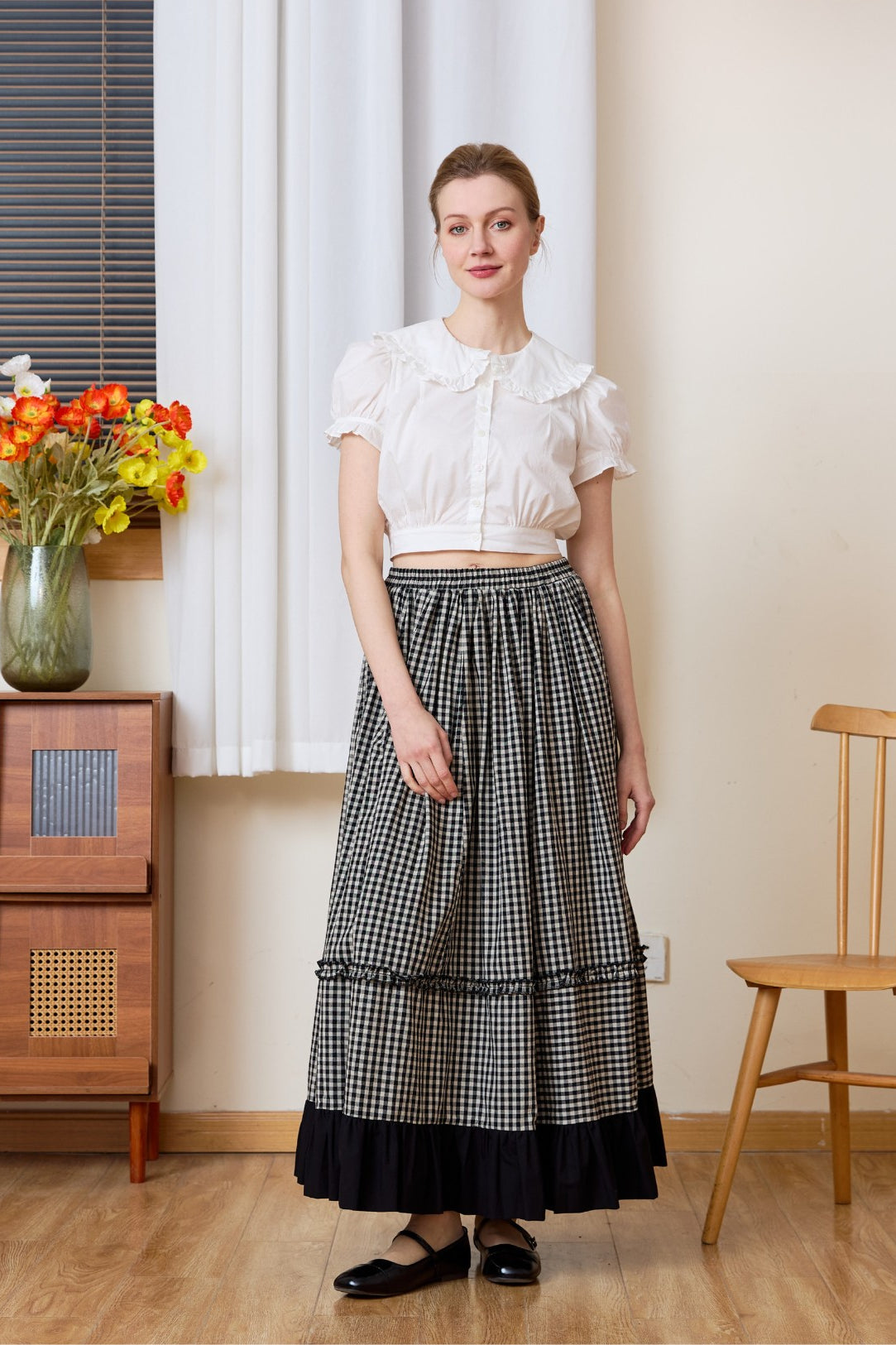 Full-length view of a woman wearing a high-waisted black and white gingham maxi skirt with a dramatic black ruffled hem, styled with a white top for a nostalgic prairie look.