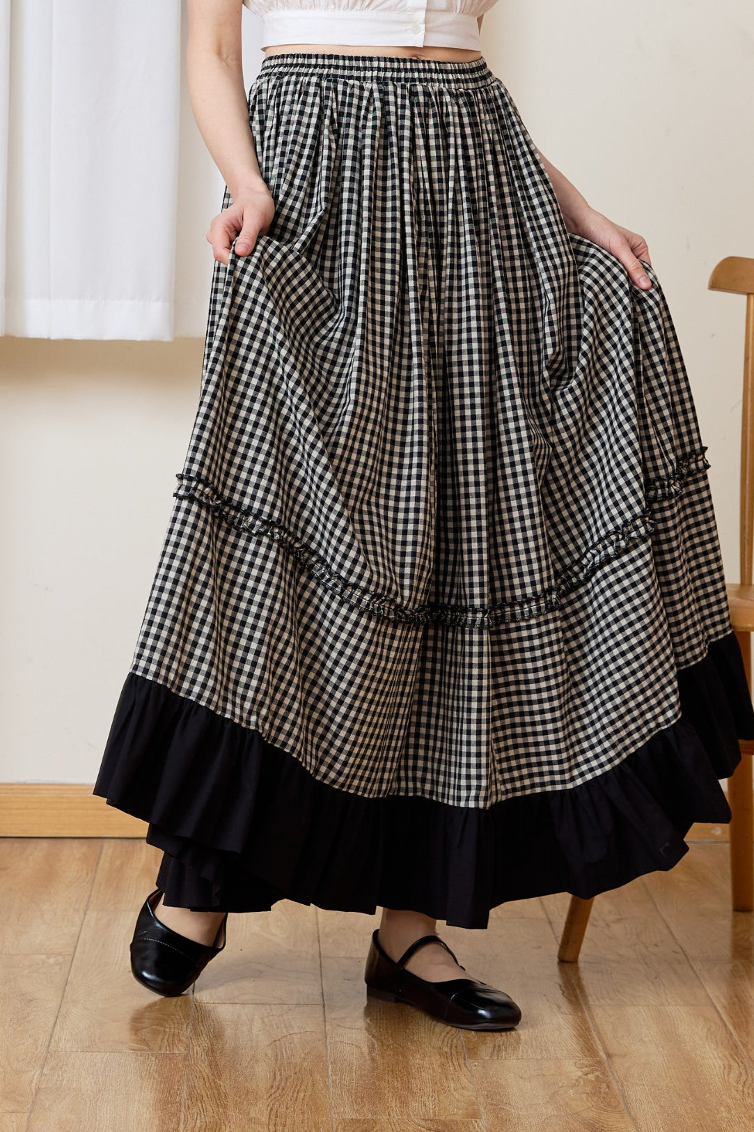 A woman holding the flowing fabric of a breathable 100% cotton gingham maxi skirt, showcasing the comfortable elastic waistband and the sweeping country-inspired silhouette.