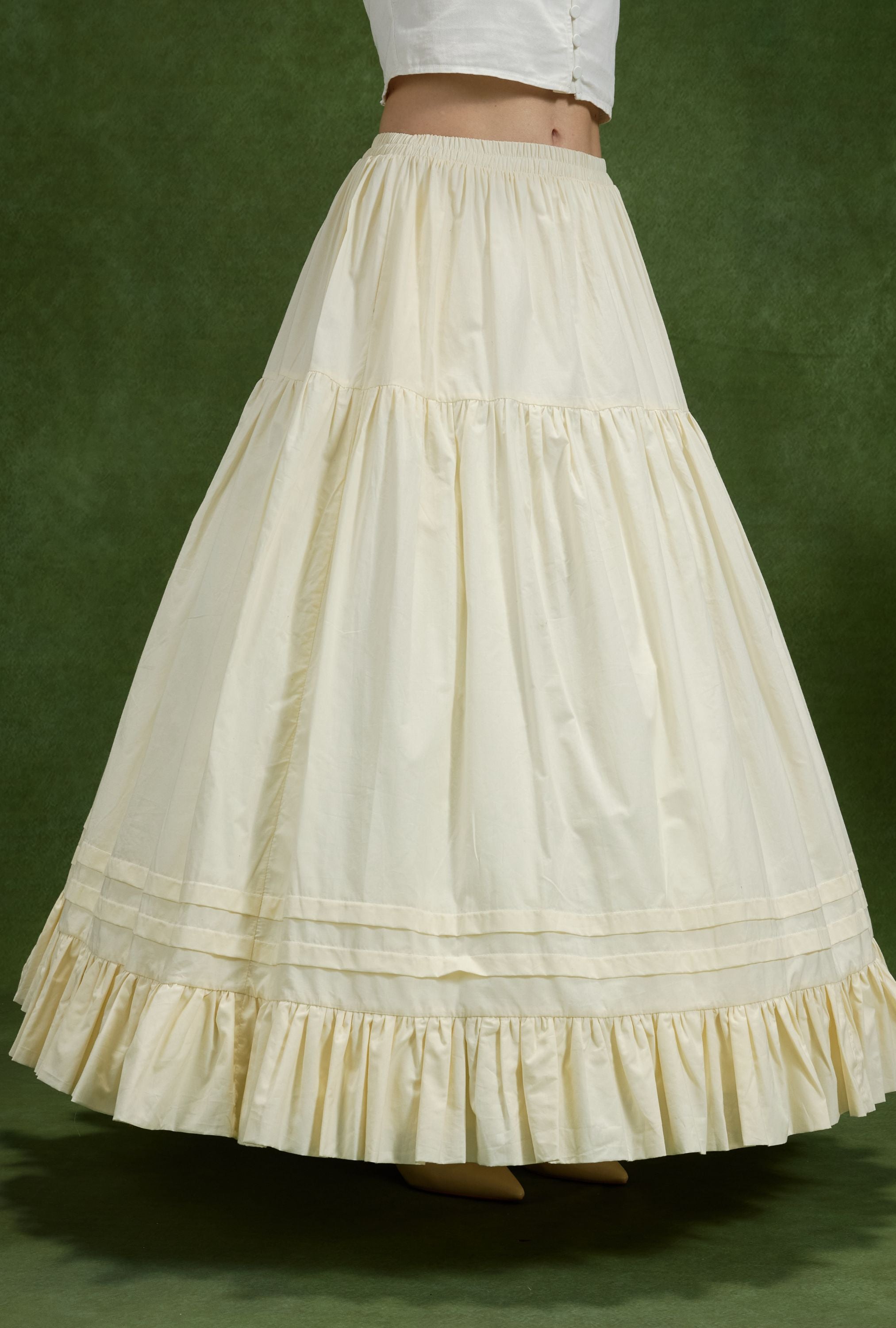 Full-length side view of a woman wearing a voluminous cream tiered cotton petticoat, its structured ball gown shape supported underneath by an ivory 4-hoop crinoline underskirt for historical cosplay dress shaping.