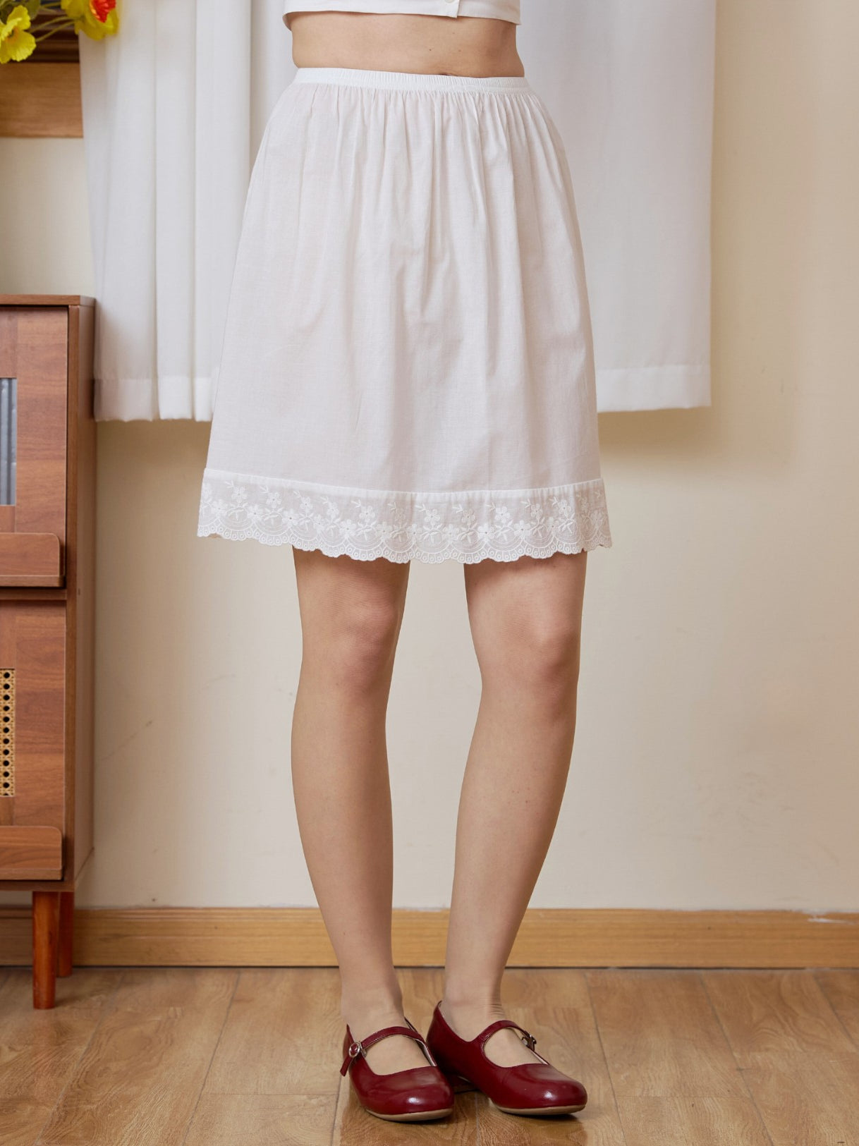 Front view of a simple vintage essential pure cotton half slip ending above the knee, paired with retro red shoes.