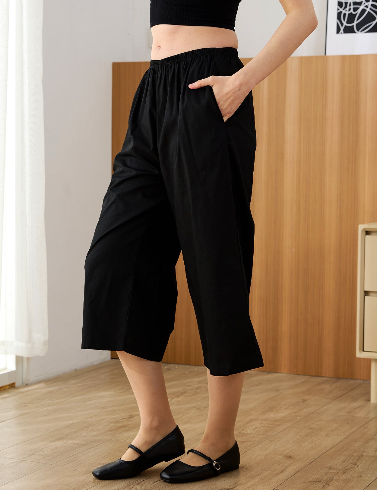 Close-up of black 100% cotton wide-leg cropped pants showing the elastic waistband and side pocket.