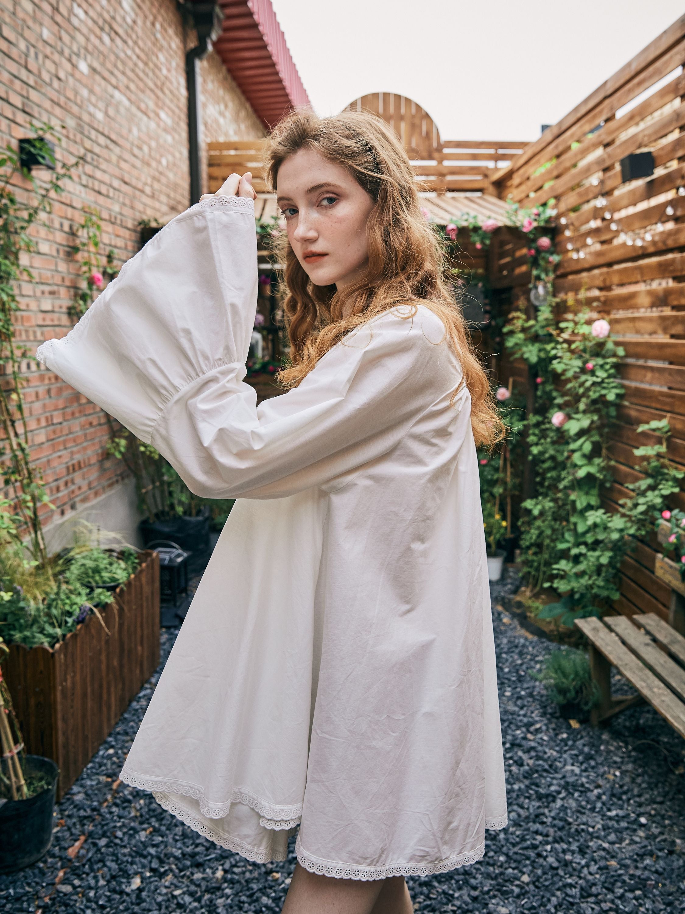 Side profile of a vintage-inspired short white cotton nightgown highlighting the draped bell sleeves and beautiful lace hem details.