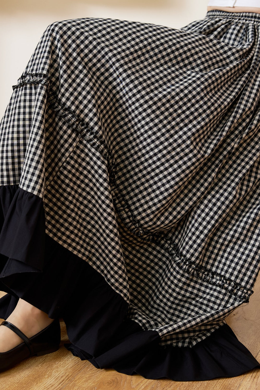 Close-up detail of a soft cotton black and white gingham maxi skirt, highlighting the delicate ruffle accents along the tiers and the striking black ruffled hemline.
