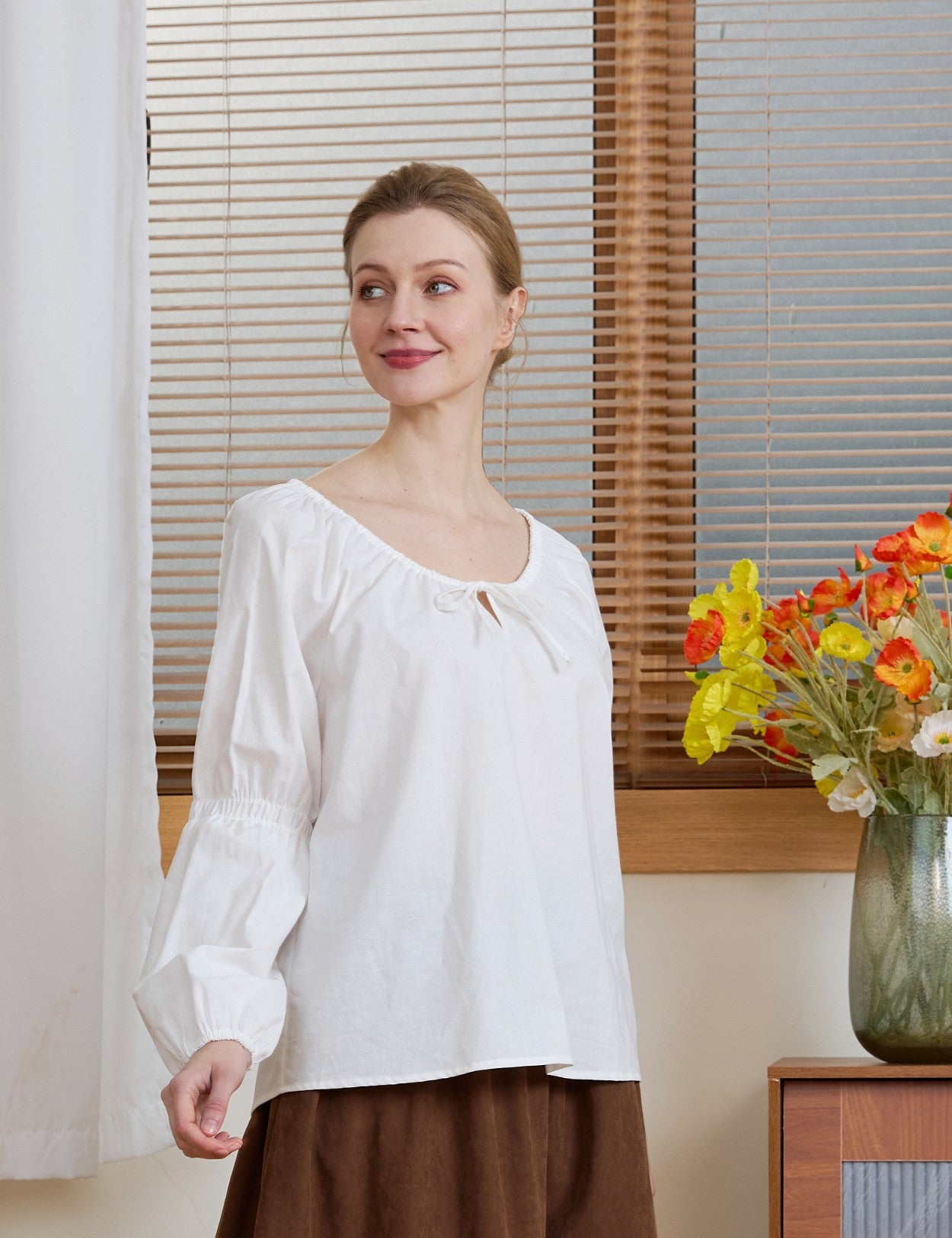 Model wearing an Ivory Renaissance Cotton Blouse, looking aside to highlight the relaxed fit and gathered sleeves.