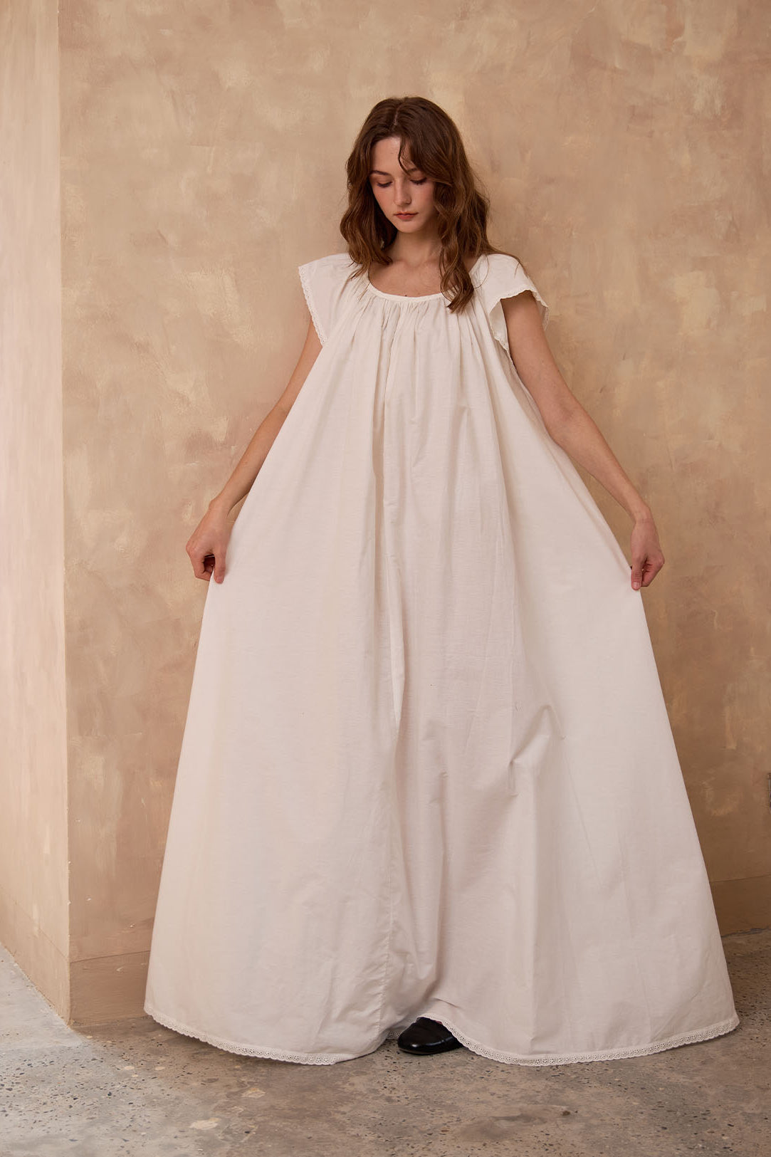 Sueasyretro floor-length ivory Victorian nightgown. Woman holding the voluminous 100% cotton skirt with lace hemline.