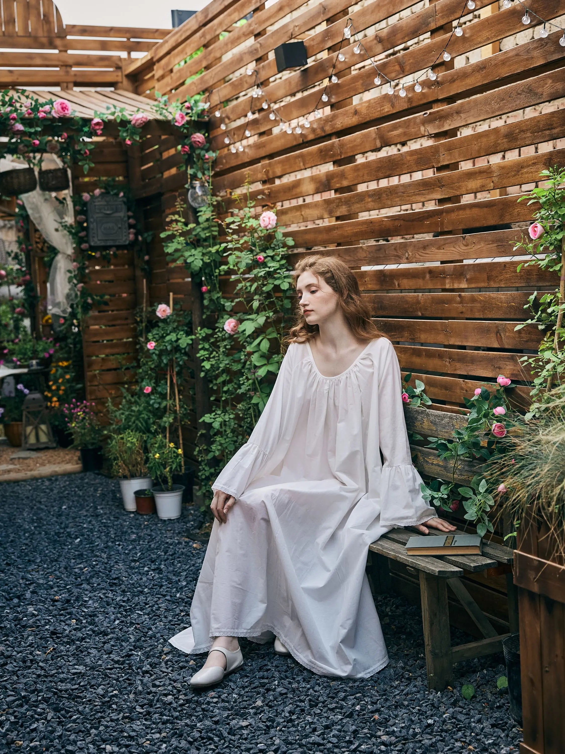 Model sitting on a garden bench wearing a white oversized vintage style nightgown.