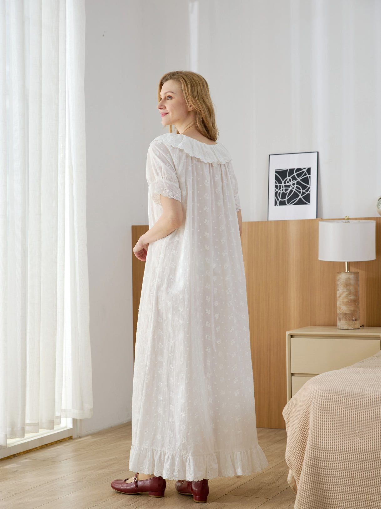 Back view of a woman modeling a flowing vintage-style cotton nightdress, showcasing the relaxed A-line fit and Broderie Anglaise ruffled hem