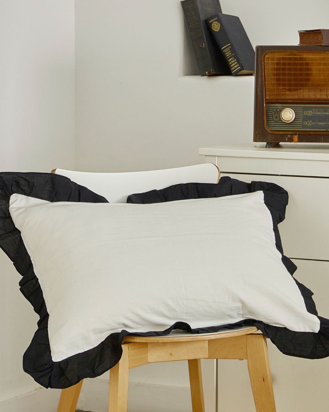 Vintage style white cotton pillow sham with black contrast ruffle trim displayed on a wooden chair for farmhouse bedroom decor