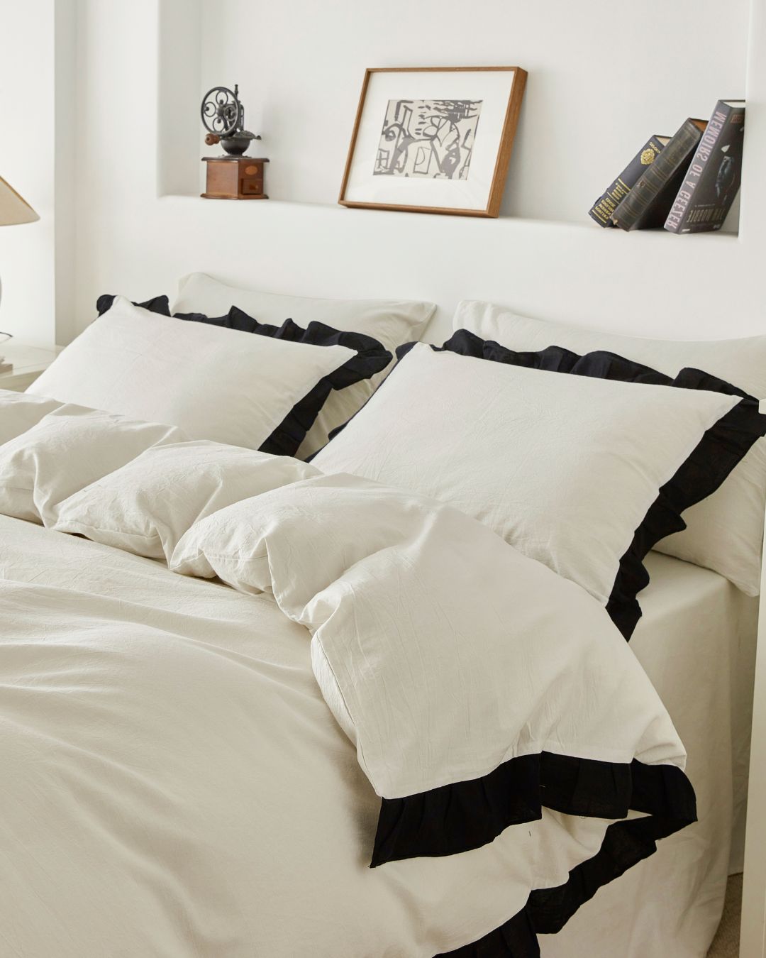 Side view close up of vintage white washed cotton bedding set featuring ruffle pillows and duvet cover with black contrast trim