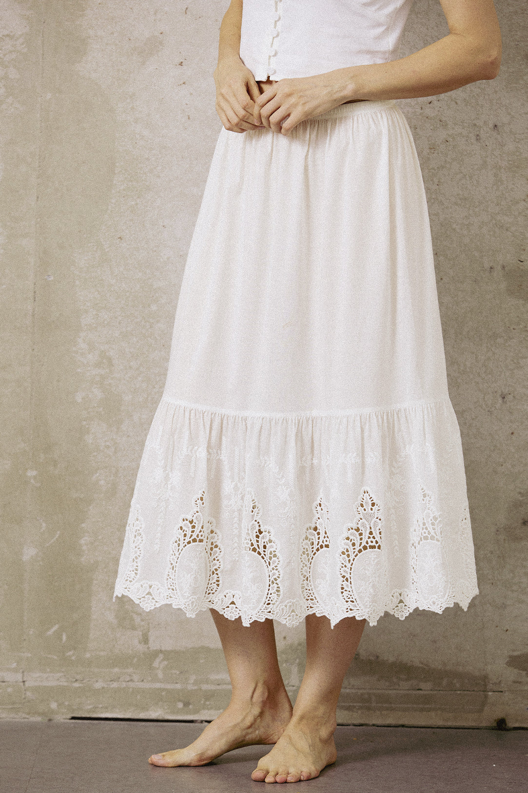 Close-up front view of a white 100% cotton mid-calf half slip with intricate embroidery lace trim at the hem.