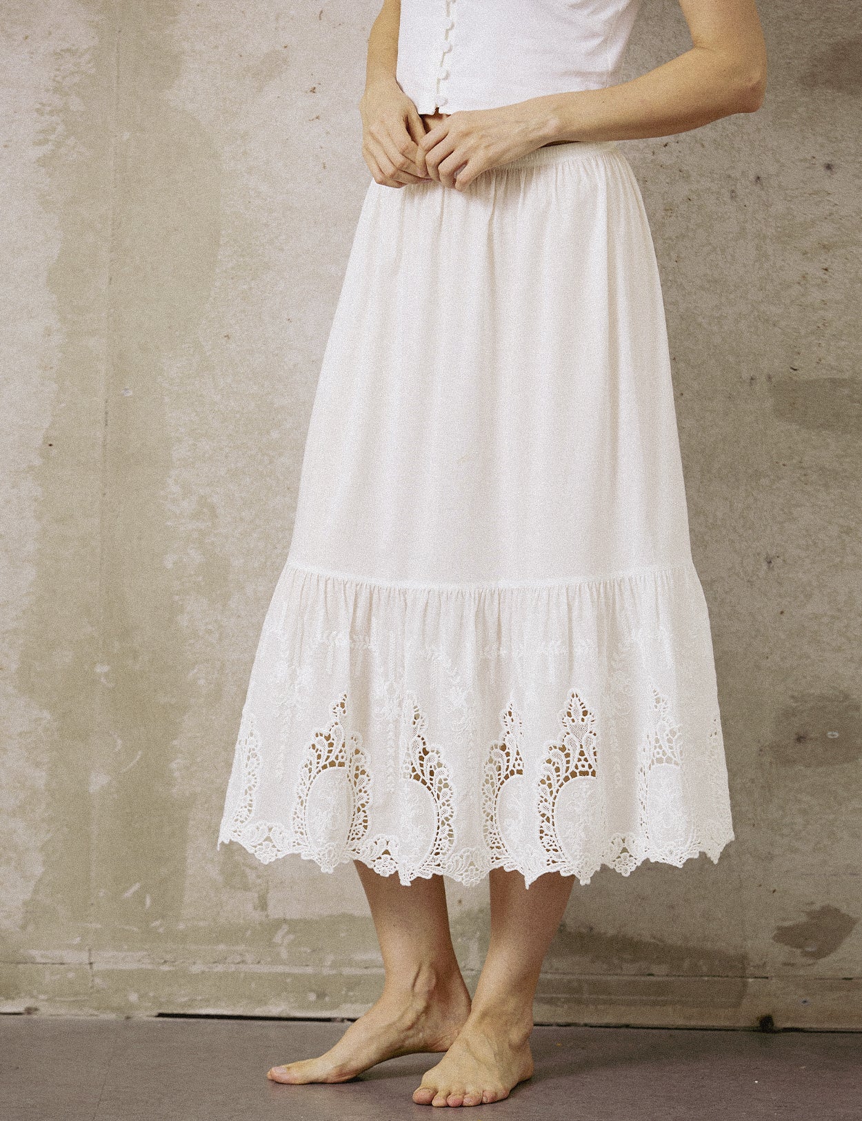 Close-up front view of a white 100% cotton mid-calf half slip with intricate embroidery lace trim at the hem.