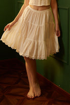 Front view of a woman wearing a breathable 22-inch knee-length cotton Victorian underskirt half slip, holding the lace-trimmed hem.