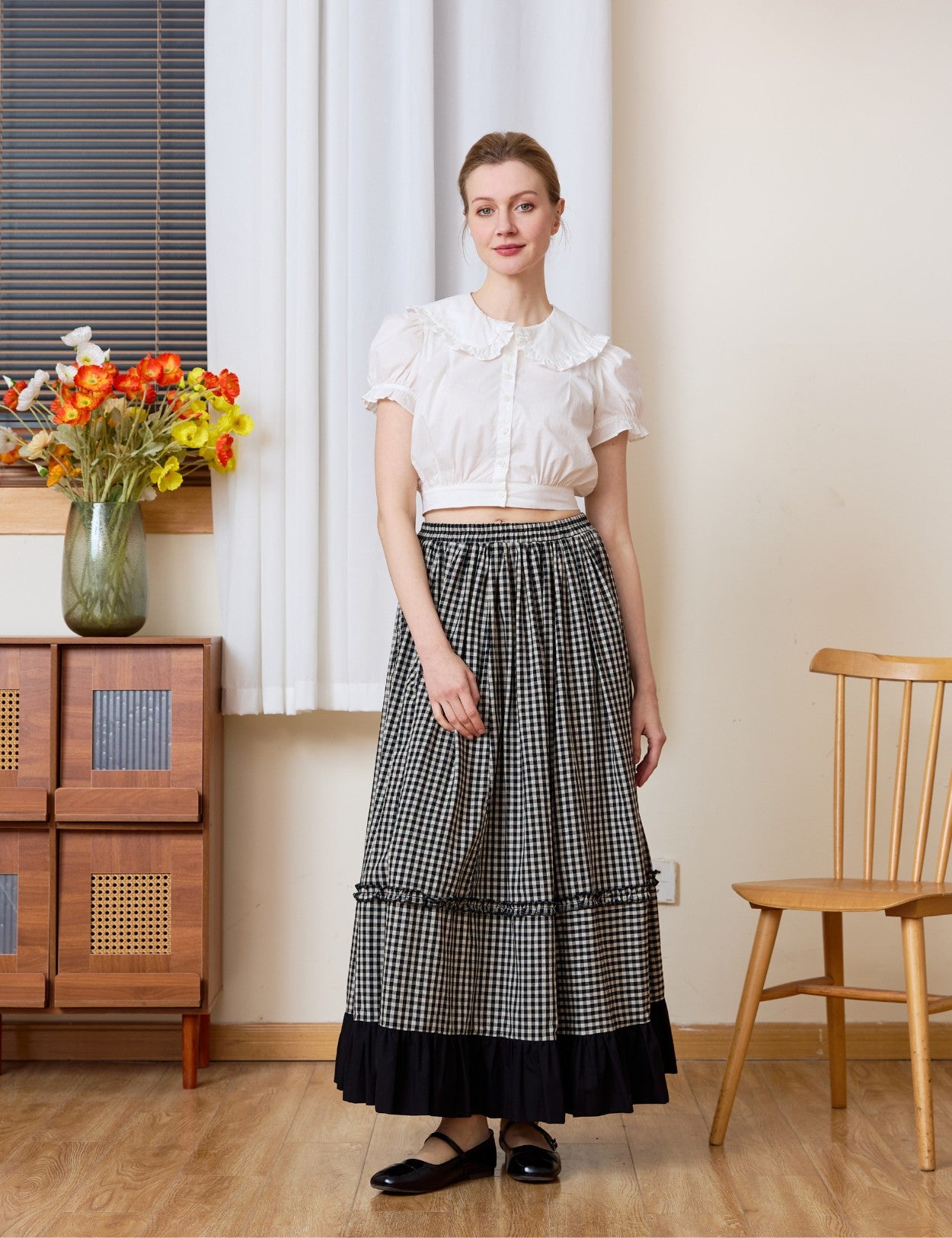 Full-length view of a woman wearing a high-waisted black and white gingham maxi skirt with a dramatic black ruffled hem, styled with a white top for a nostalgic prairie look.