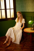 Seated woman styling a long handmade cotton petticoat as an elegant vintage skirt, highlighting the voluminous drape and breathable fabric in a retro setting.
