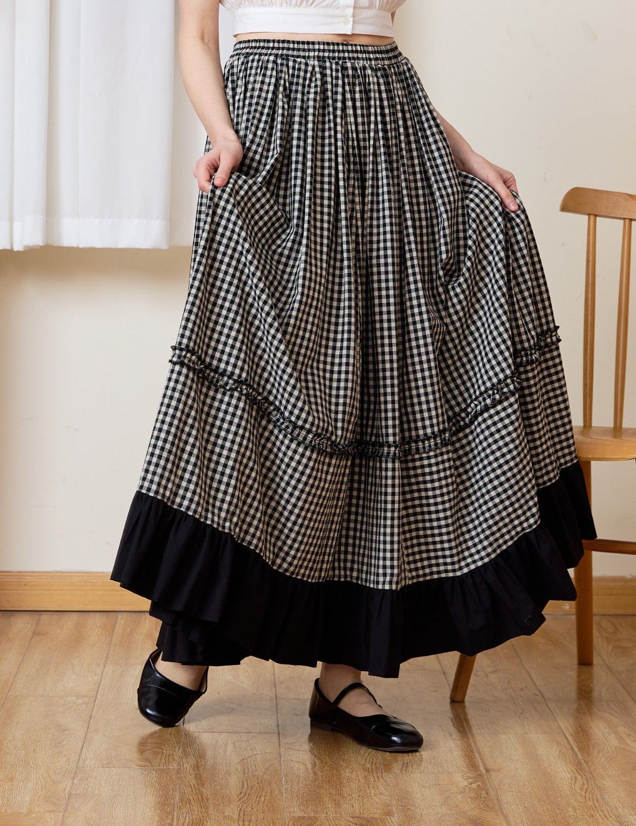 A woman holding the flowing fabric of a breathable 100% cotton gingham maxi skirt, showcasing the comfortable elastic waistband and the sweeping country-inspired silhouette.