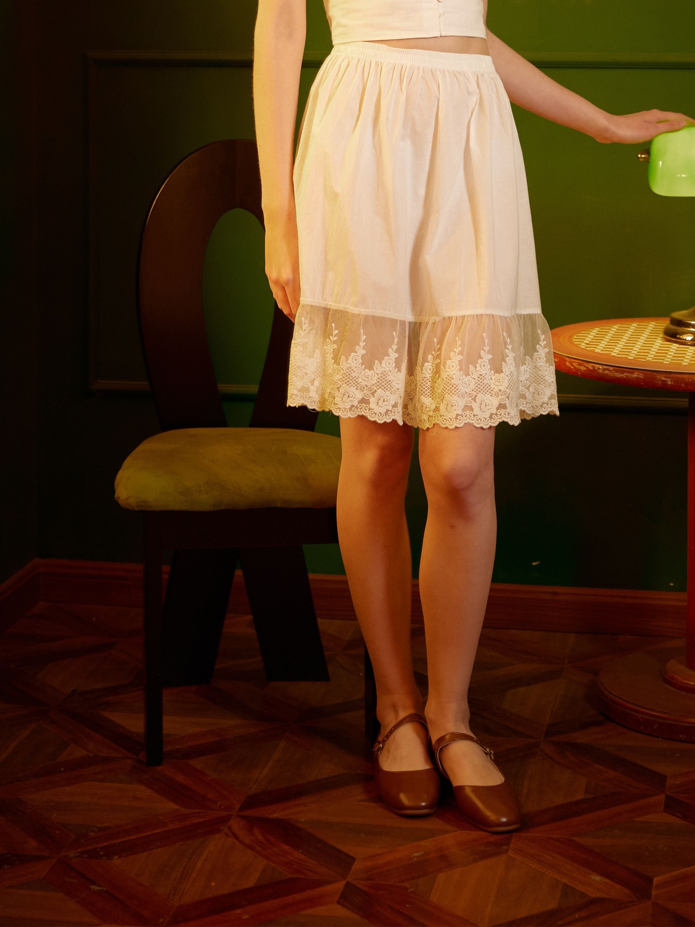 Close-up of a versatile white cotton skirt extender, highlighting the comfortable elastic waistband and the delicate feminine floral lace bottom section.