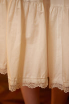  Close-up detail of the pure cotton half slip fabric, showing the gentle gathers, tiered seams, and exquisite floral lace trim at the hemline.
