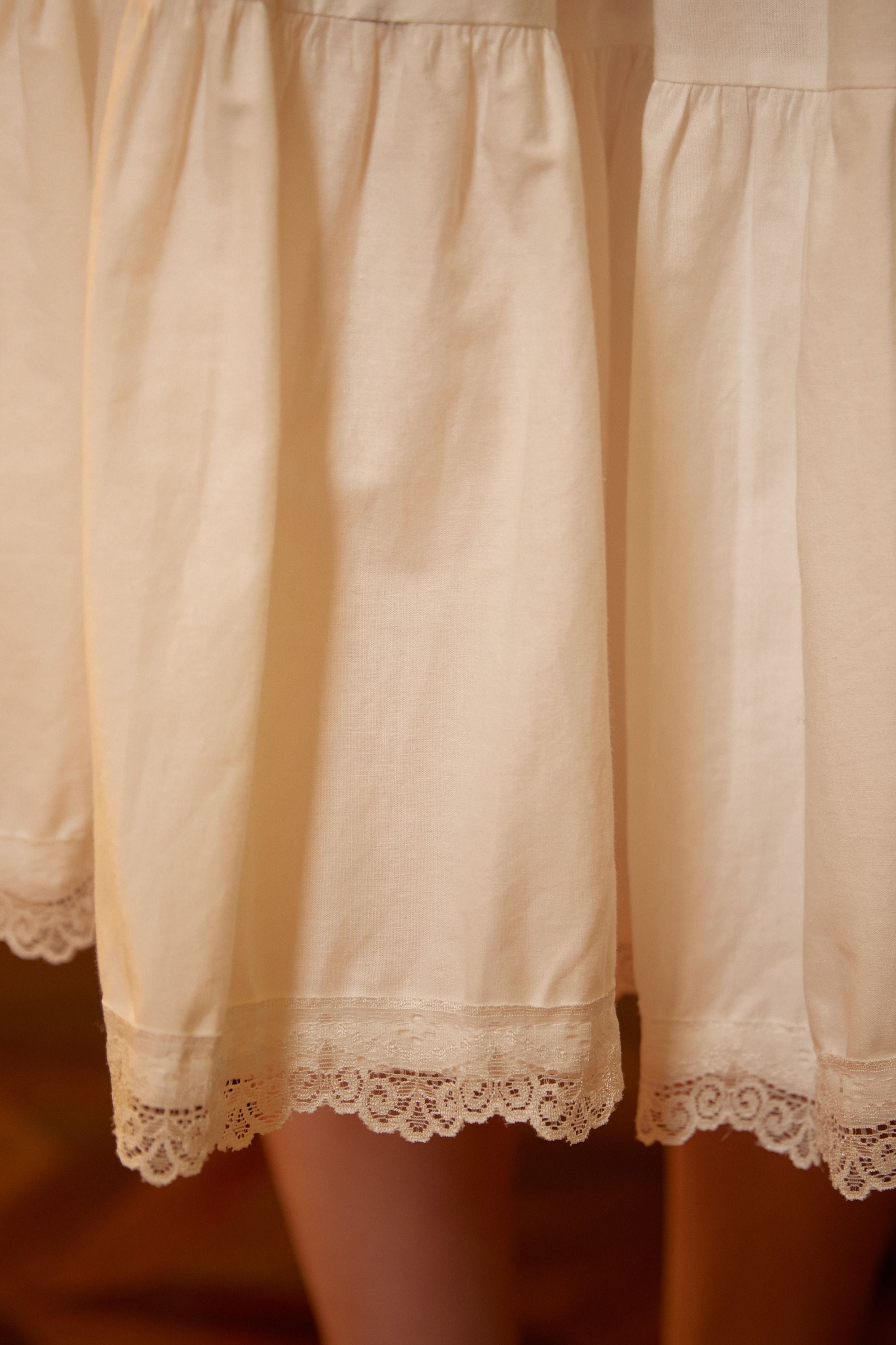  Close-up detail of the pure cotton half slip fabric, showing the gentle gathers, tiered seams, and exquisite floral lace trim at the hemline.
