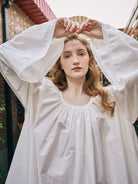 Close-up of the elegant gathered neckline and delicate lace trim on the bell sleeves of a handmade white pure cotton chemise sleepwear.