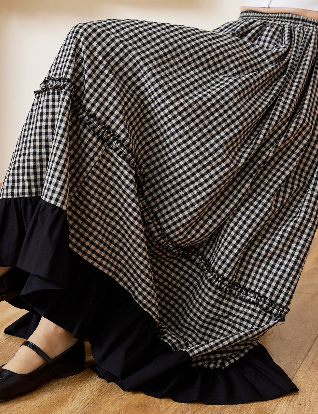 Close-up detail of a soft cotton black and white gingham maxi skirt, highlighting the delicate ruffle accents along the tiers and the striking black ruffled hemline.