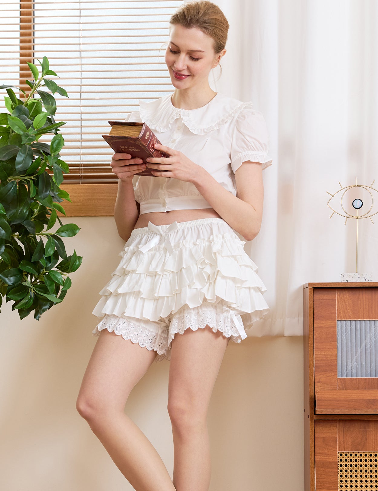 Woman relaxing with a book wearing Victorian-inspired white ruffle lace shorts, styled as breathable cotton loungewear for an effortless everyday vintage look.