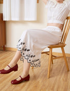 Model sitting to display the hem of the white cotton Petticoat with bluework details.