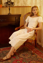 Model sitting in a garden wearing Sueasyretro Victorian cotton bloomers. Elegant bloomer femme style with eyelet details.