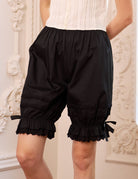 Close-up of the black cotton bloomers. Shows eyelet lace pintucks, soft ruffles, and satin bows on these bloomer pants.