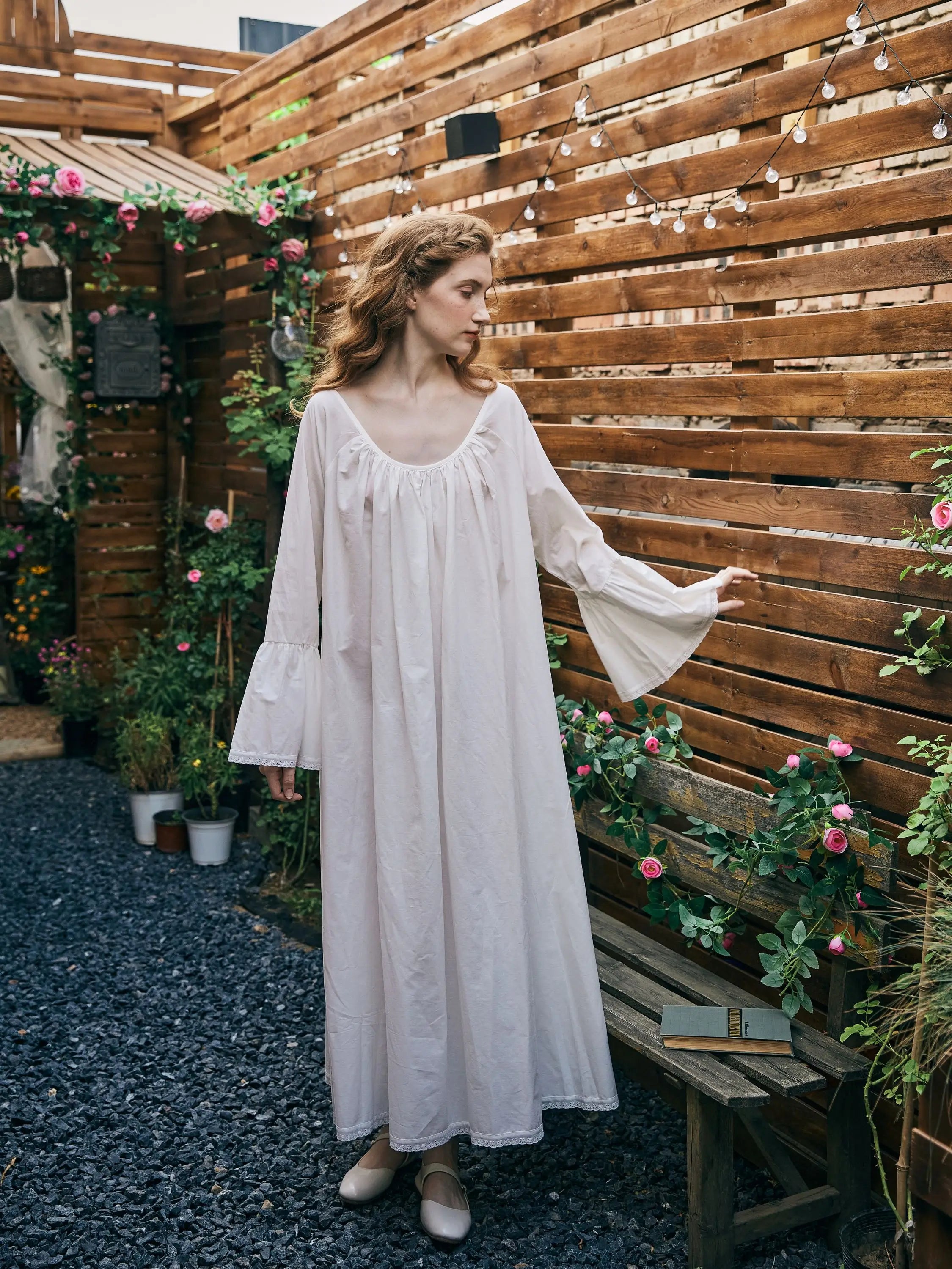 Elegant bell sleeve Victorian nightgown displayed by a model in a vintage garden setting.