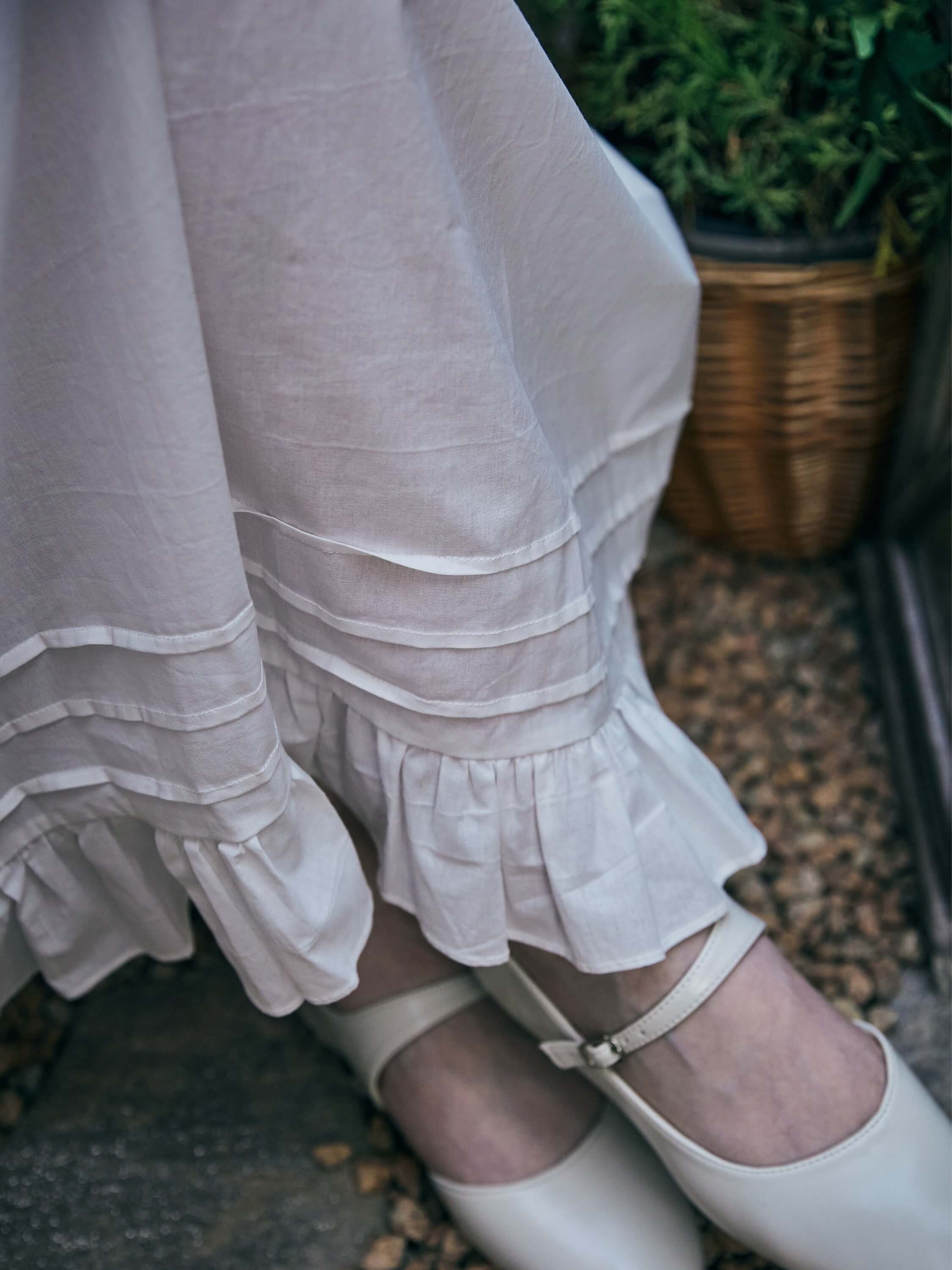 Texture detail of the white cotton fabric showing horizontal pintucks and a ruffled hemline on the Ophelia Edwardian nightgown.