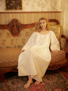 Woman relaxing on an antique sofa wearing a romantic peasant style long cotton sleepwear.