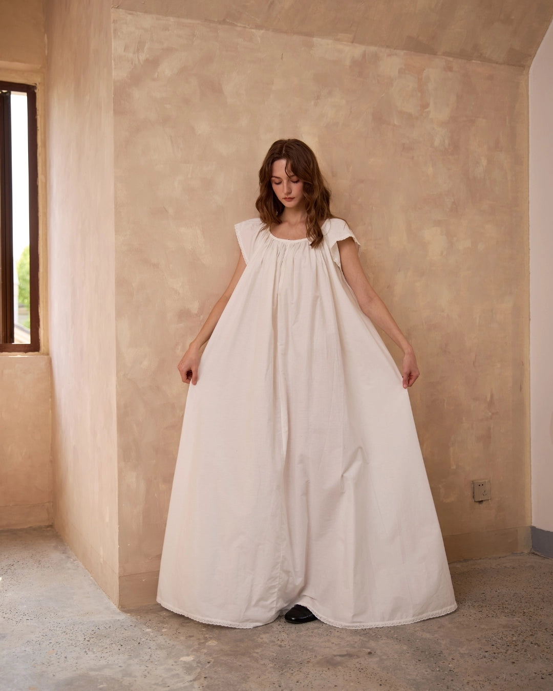 Woman in a romantic vintage-style ivory Victorian cotton nightgown with sleeveless lace-trim shoulders.