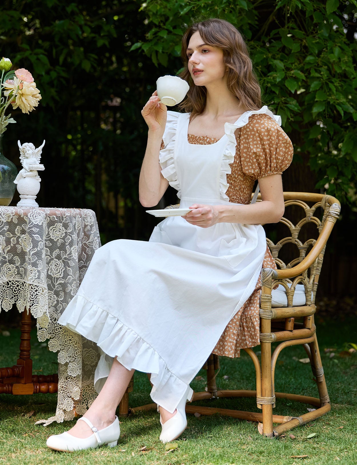 Woman in Victorian cotton pinafore apron enjoying tea in garden