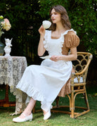 Woman in Victorian cotton pinafore apron enjoying tea in garden