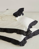 Stack of folded vintage white washed cotton bedding set including duvet cover and pillowcases with black contrast ruffles
