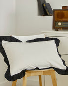 Vintage style white cotton pillow sham with black contrast ruffle trim displayed on a wooden chair for farmhouse bedroom decor