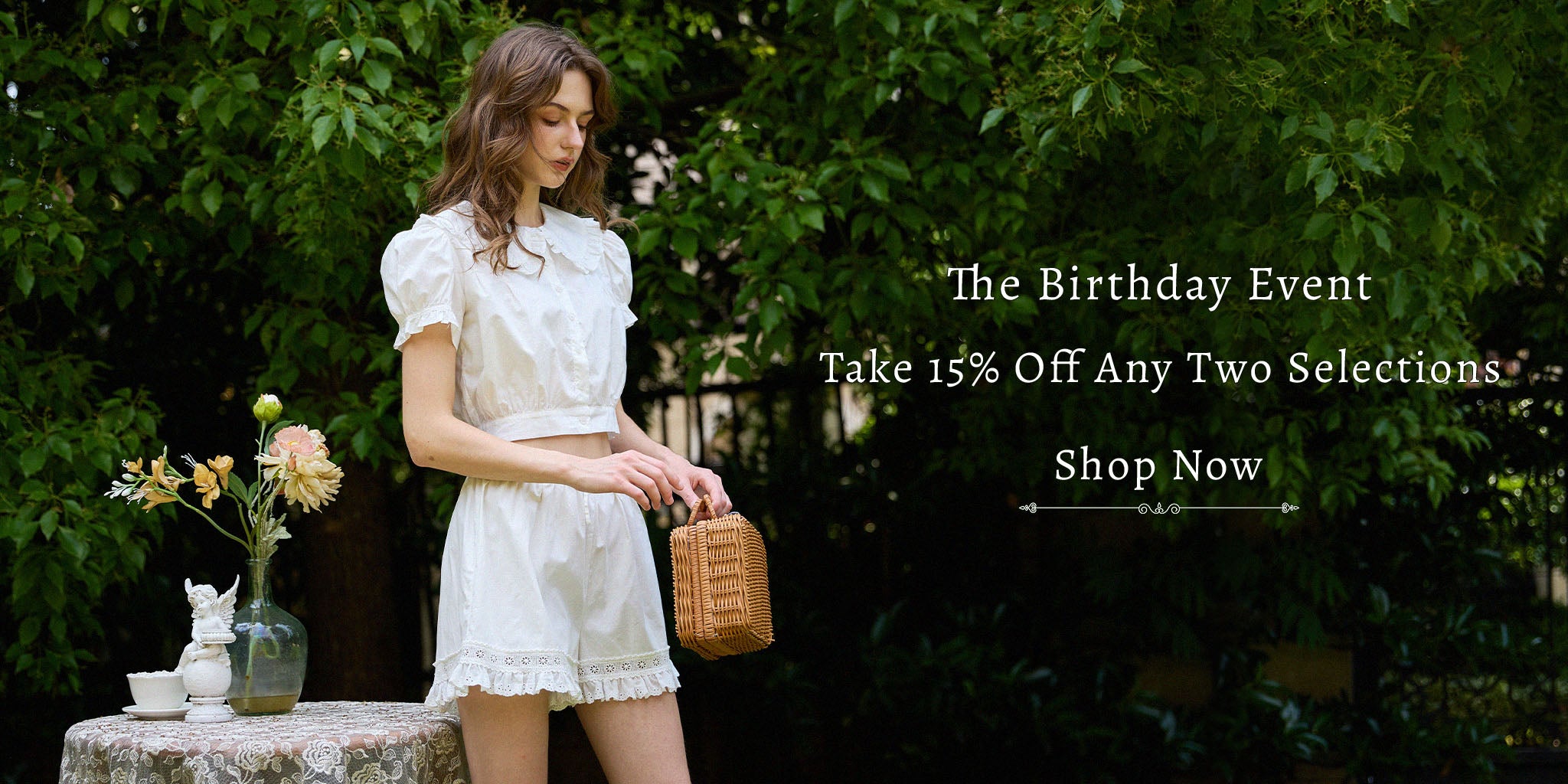 A model wearing a white vintage-inspired pure cotton two-piece set with a Peter Pan collar, standing outdoors against lush green foliage.